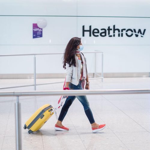 A woman is waking at the Heathrow Airport along yellow rolling bag
